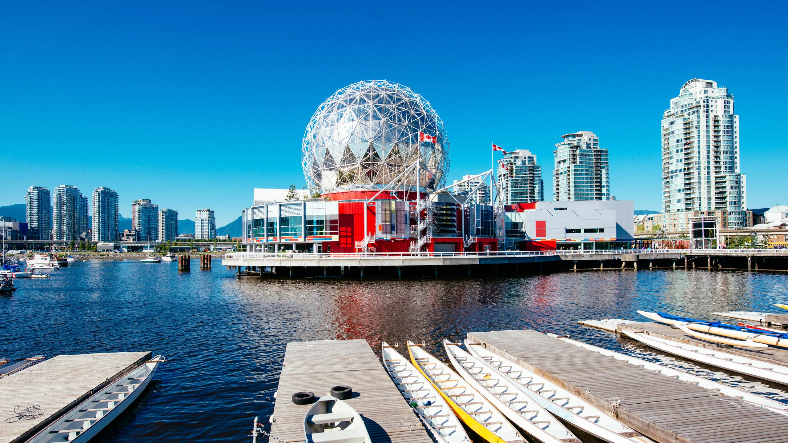 Vancouver BC skyline with glass towers, mountains, and water from False Creek